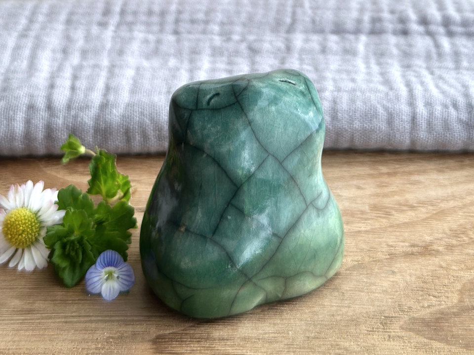 a happy frog raku ceramic sculpture glazed in green at the bottom and forest green everywhere else. it has a kind, happy face and is a lovely shape to hold in the hand.