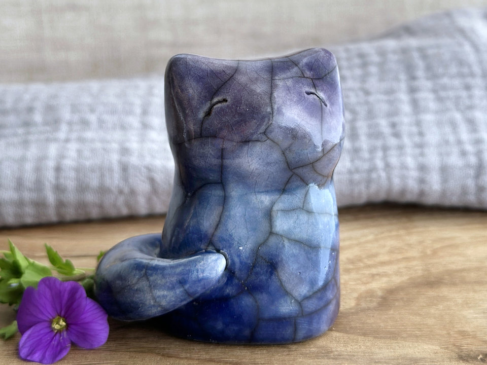 A calm and gentle Shinto Inari nighttime kitsune fox spirit ceramic raku statue glazed in a bottom-to-top gradient of dark blue to blue to purple. Its tail is curled around the right side of its body, and it has a kind face.