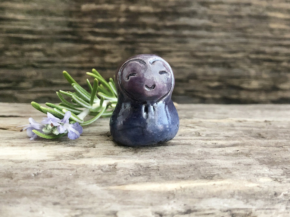 A smiley and loving Jizo Shinto raku ceramic sculpture talisman glazed in indigo and violet colours with a heart shape around his kind, smiling face.