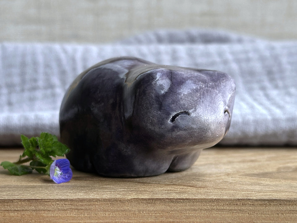 Ceramic raku bear kami sculpture glazed in grey violet with darker violet on its right side. It has a kind, gentle face and is a little chonky.