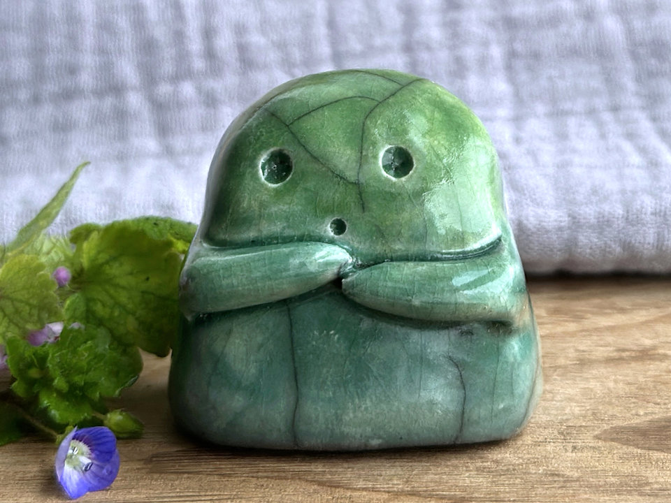 A sweet little kodama nature spirit ceramic guardian statue glazed in shades of green and with a lovely, gentle face and little arms.
