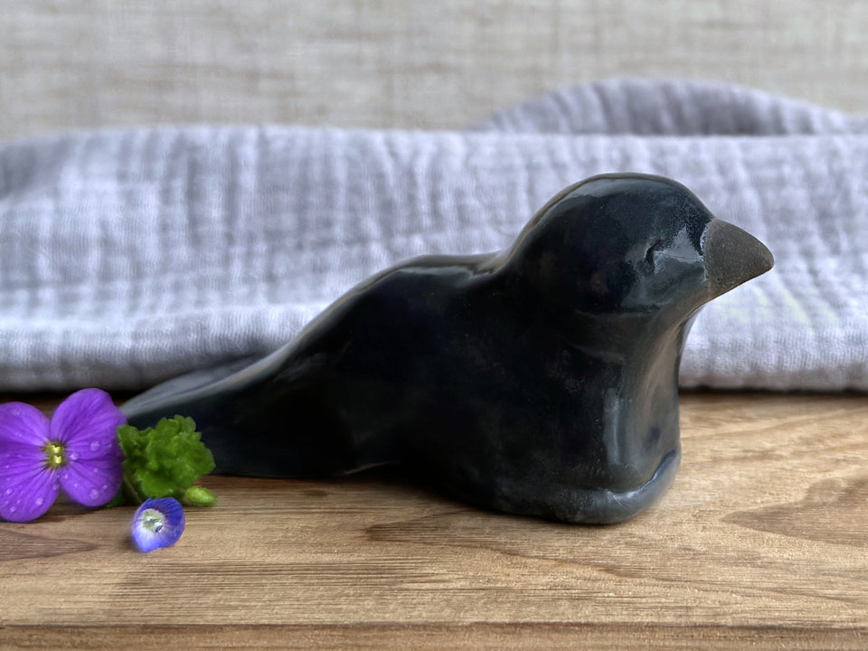  Raku ceramic sculpture of a sitting raven. It is glazed in dark blue-grey, and its beak is left natural, unglazed black.