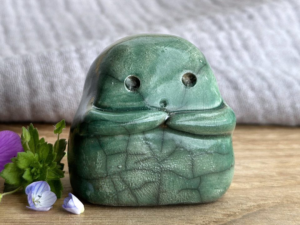 A sweet little kodama nature spirit ceramic guardian statue glazed in shades of green and with a lovely, gentle face and little arms. Its tummy is gently textured.