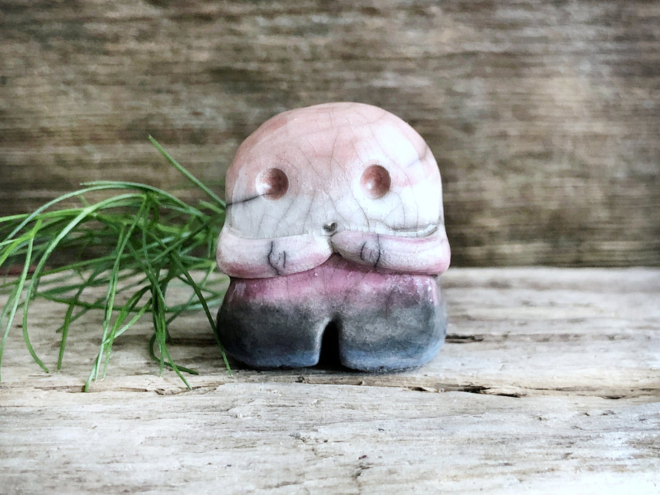 A sweet little nature spirit ceramic guardian statue glazed in the genderfluid flag pink, white, purple, black, and blue colours and with a lovely, gentle face and little arms. It has a small branch design carved up one side.