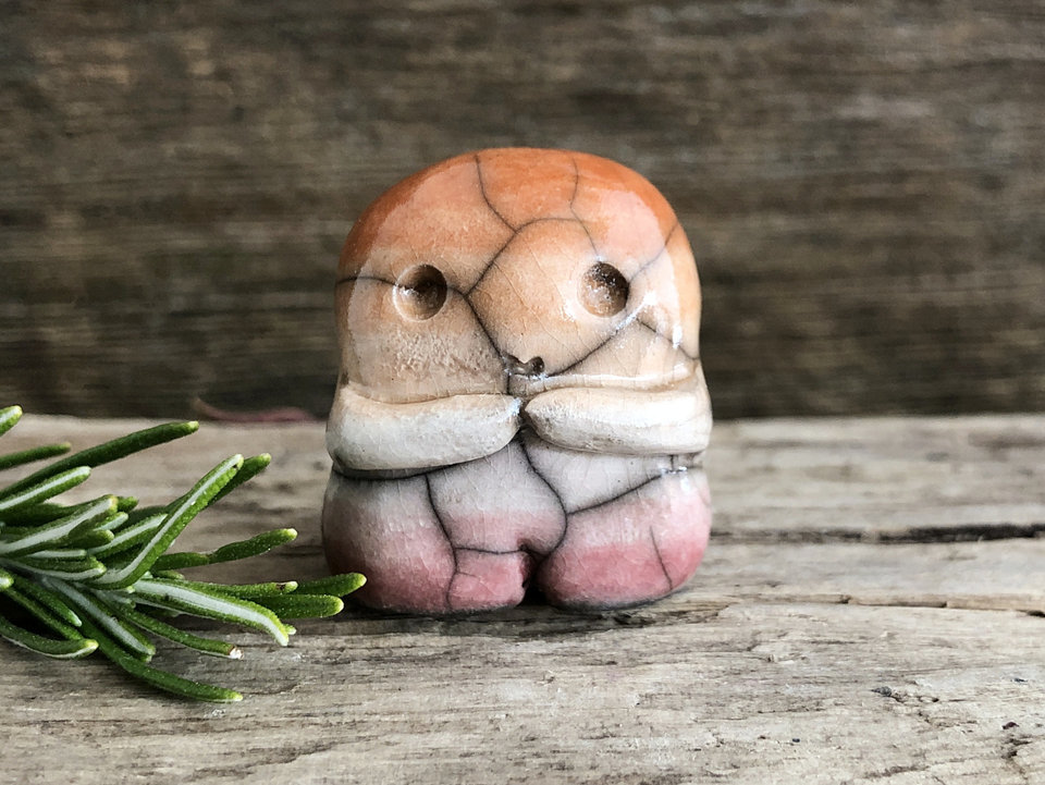 A sweet little nature spirit ceramic guardian statue glazed in the lesbian orange, white, and pink colours and with a lovely, gentle face and little arms. It has a small branch design carved up one side.