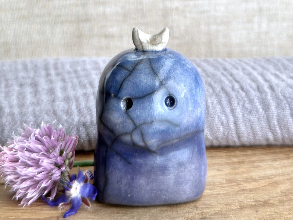 A kodama nature and forest spirit kami ceramic raku sculpture glazed in a bottom-to-top gradient of indigo-violet to blue. It has a gentle face, and a white crescent moon on its head.
