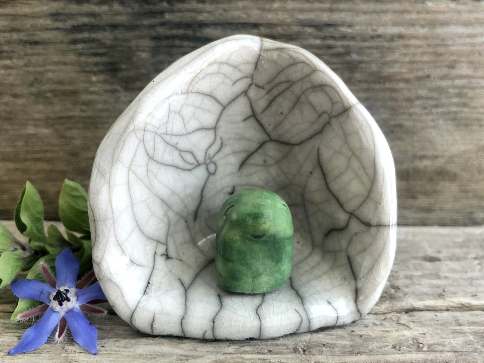 A Shinto kodama nature spirit kami of forests and trees in his own little kamidana shine. The kodama has a very sweet face and is glazed in green. The shrine is white with beautiful raku patterns and vaguely egg-shaped.