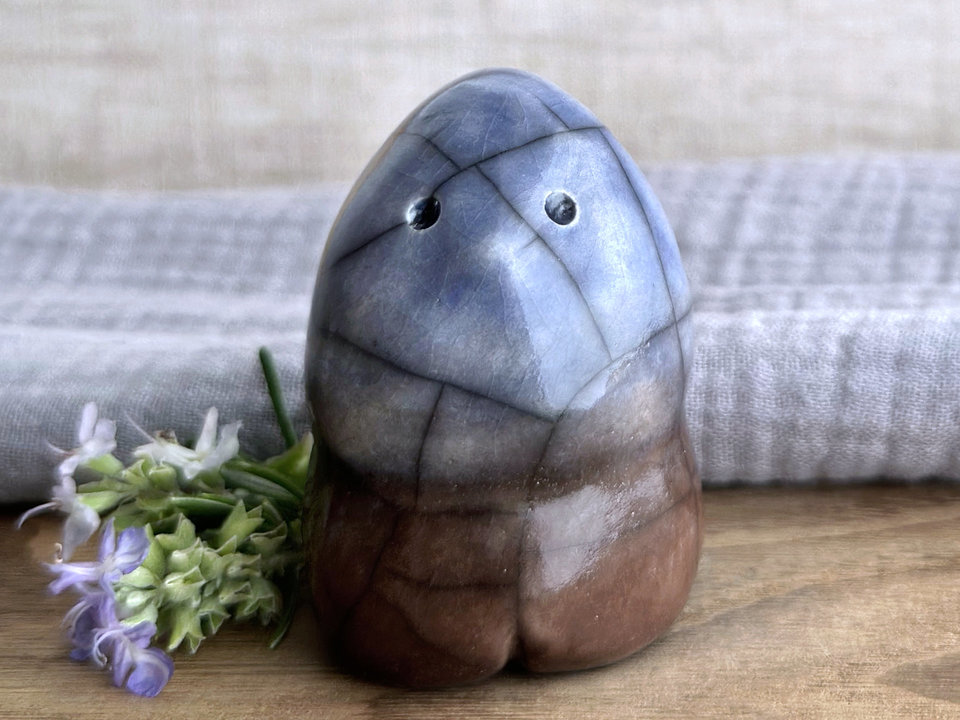 a vaguely dome-shaped nature spirit ceramic sculpture with a gently pointed head and four stubby little legs. it is glazed in a bottom-to-top gradient of brown to blue and has a gentle face with two round eyes and a stubby nose.