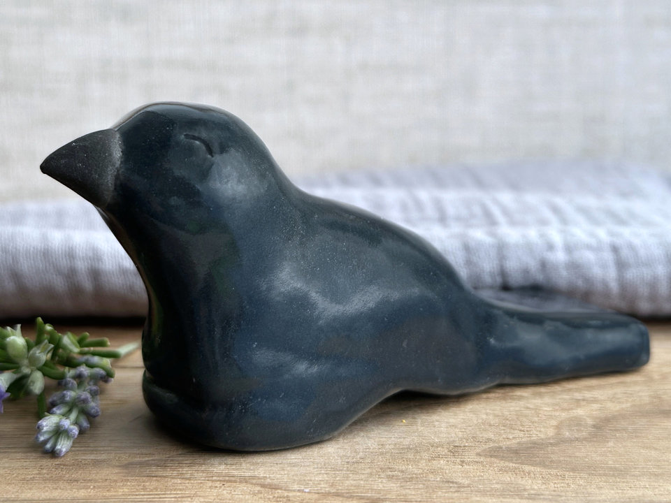 a sitting crow and raven sculpture glazed in a dark blue-black colour. its beak is natural unglazed black. it has gently smiling eyes and looks like a friend.
