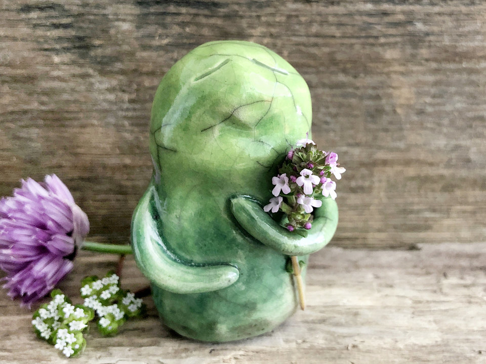 raku ceramic earth spirit warrior sculpture. it is glazed in a gradient from darker to lighter green (bottom to top) and has two cute little arms. it has a quiet, sleepy expression on its gentle face.