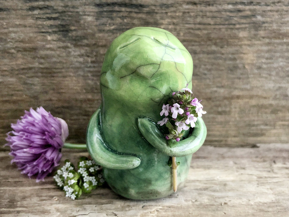 raku ceramic earth spirit warrior sculpture. it is glazed in a gradient from darker to lighter green (bottom to top) and has two cute little arms. it has a quiet, sleepy expression on its gentle face.