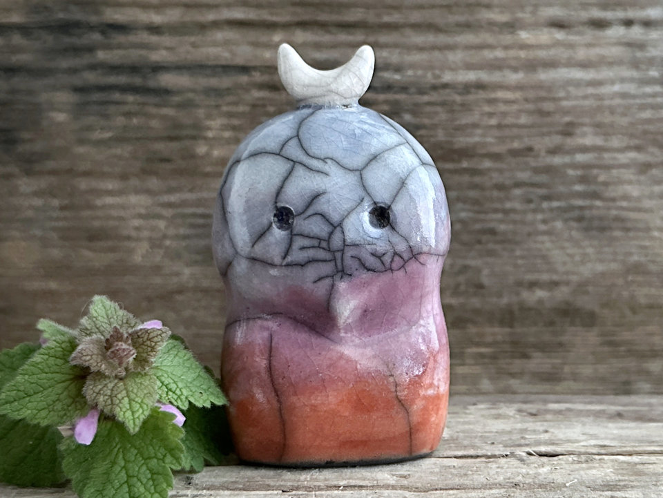 A kodama nature and forest spirit kami ceramic raku sculpture glazed in a bottom-to-top gradient of burnt red-orange to mauve to purple to indigo. It has a gentle face, and a white crescent moon on its head.