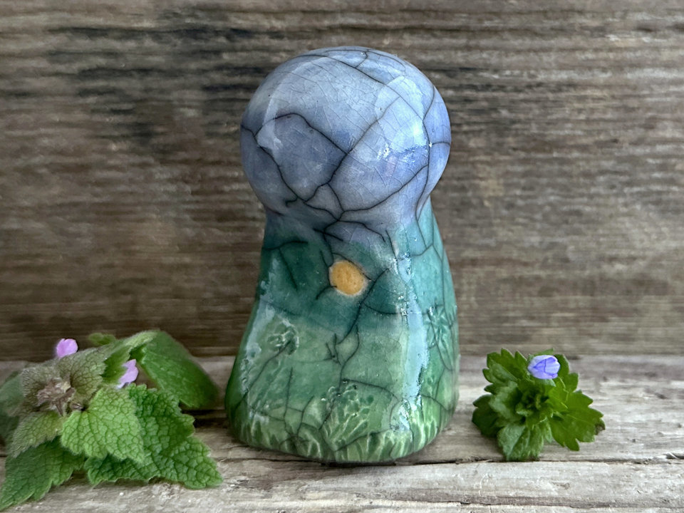 Raku ceramic mother earth spirit spirit sculpture glazed in spring green, forest green, and blue (bottom to top). It has plant shapes and flowers carved into it and a yellow sun carving too.