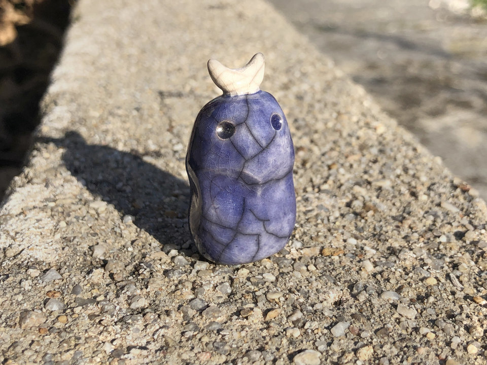 A sweet, tiny kodama nature and forest spirit kami ceramic raku sculpture glazed in indigo and violet with a gentle face and a crescent moon on its head.