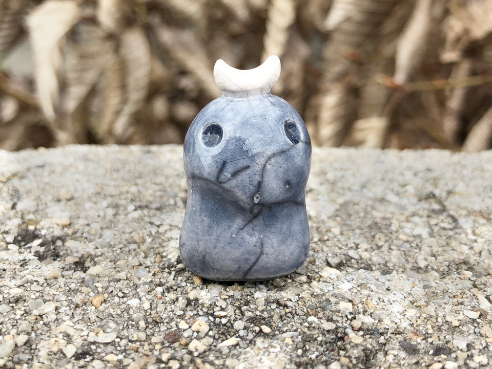 A sweet little kodama nature and forest spirit kami ceramic raku sculpture glazed in pale grey-blue with a gentle face and a crescent moon on its head.