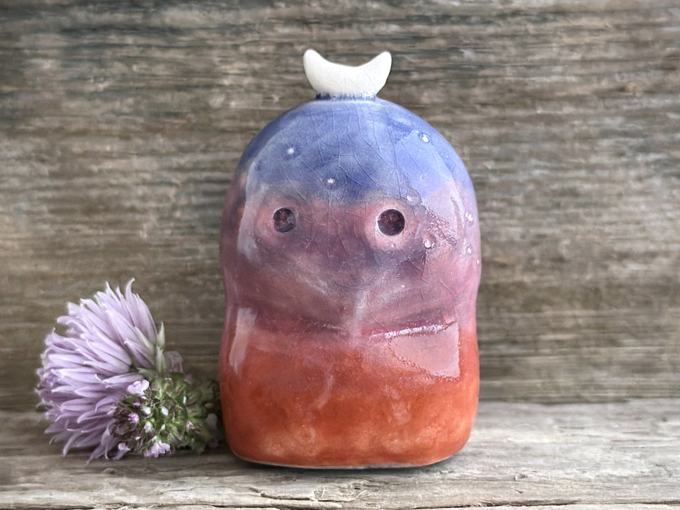 A kodama nature and forest spirit kami ceramic raku sculpture glazed in a bottom-to-top gradient of burnt red-orange to mauve to purple to indigo. It has a gentle face, some small white marks like stars on its head, and a white crescent moon on top.