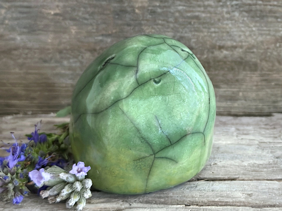 vaguely egg-shaped but quite round and stout nature spirit sculpture. it is glazed in a bottom-to-top gradient of yellow-green to spring green and looks a little like a frog. it has a gentle, happy face.