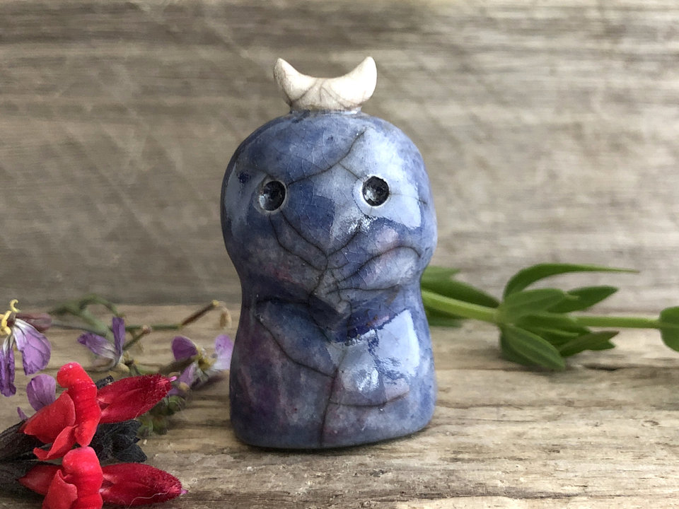 A kodama nature and forest spirit kami ceramic raku sculpture glazed in blue and a touch of soft red with a gentle face and a crescent moon on its head.