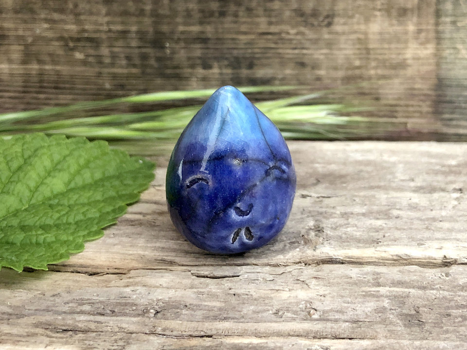 A small raindrop raku ceramic sculpture in blue and turquoise with a very smiley face! A prayer to end the droughts and floods and restore balance.