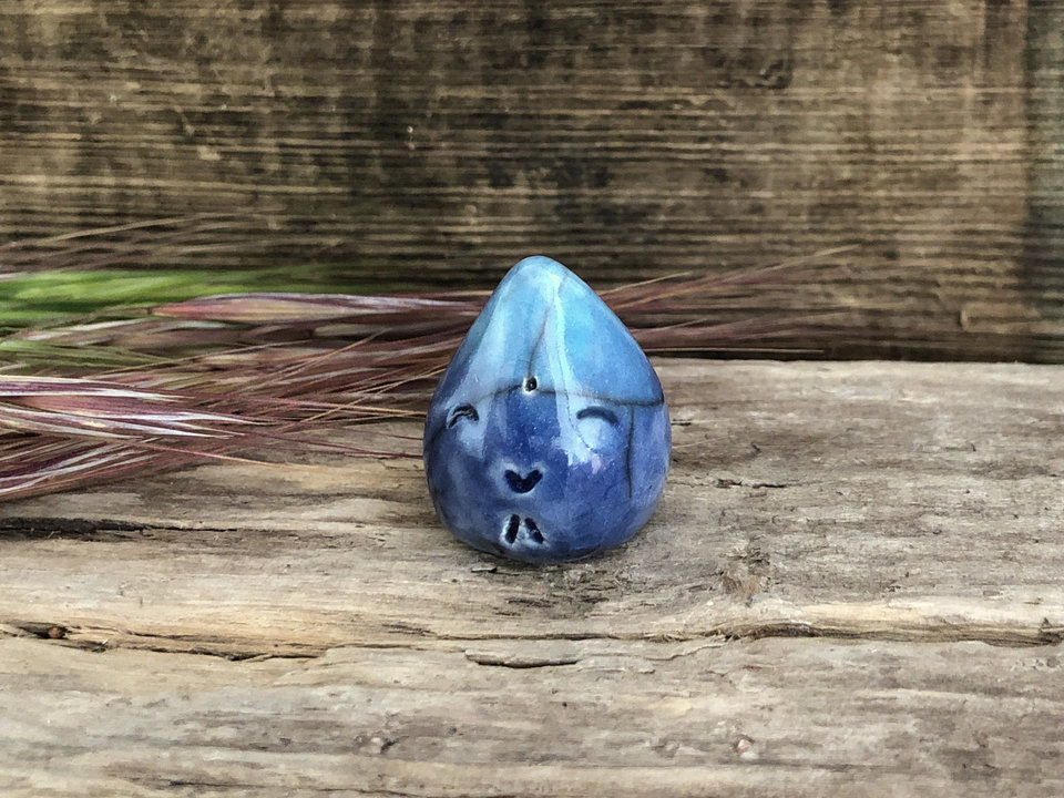 A very small raindrop raku ceramic sculpture glazed in blue and turquoise with a smiley face. A prayer to end the droughts and floods.