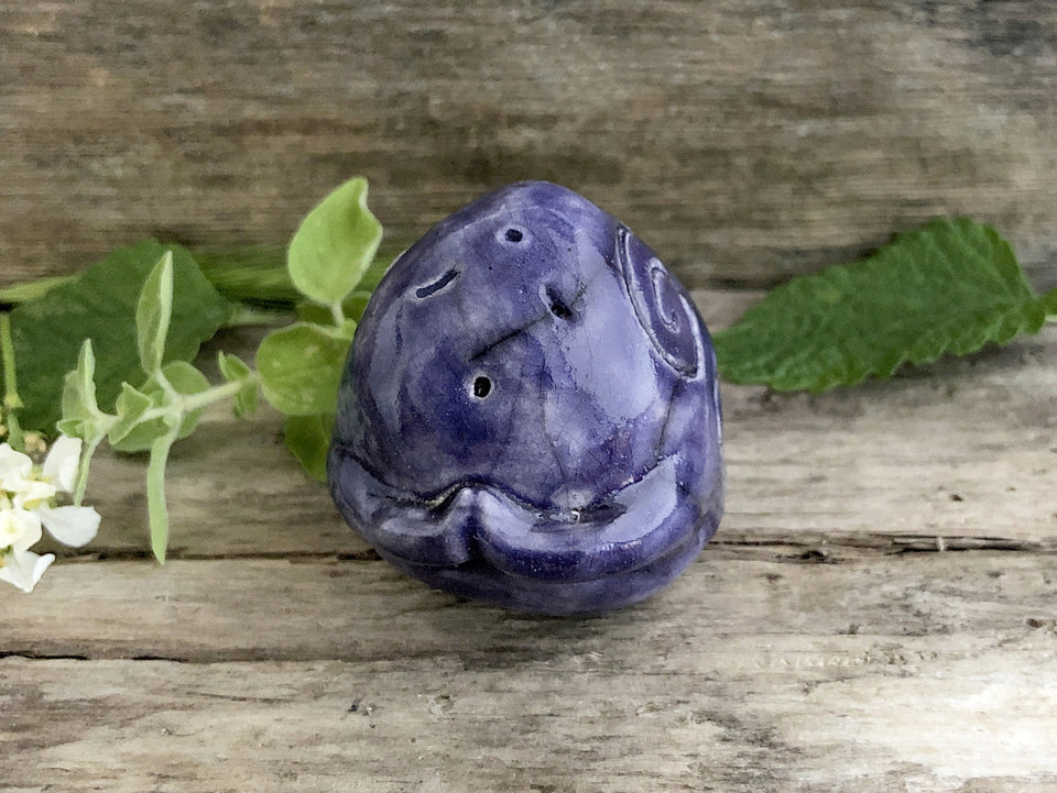 Almost round ceramic sculpture of an elemental stone spirit gnome. He has a sweet face and a little open mouth and glazed in violet with Celtic spiral decorations.