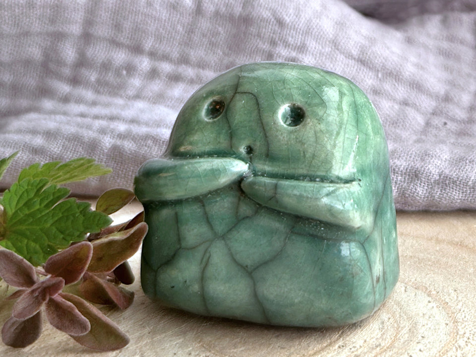 A sweet little kodama nature spirit ceramic guardian statue glazed in shades of green and with a lovely, gentle face and little arms.
