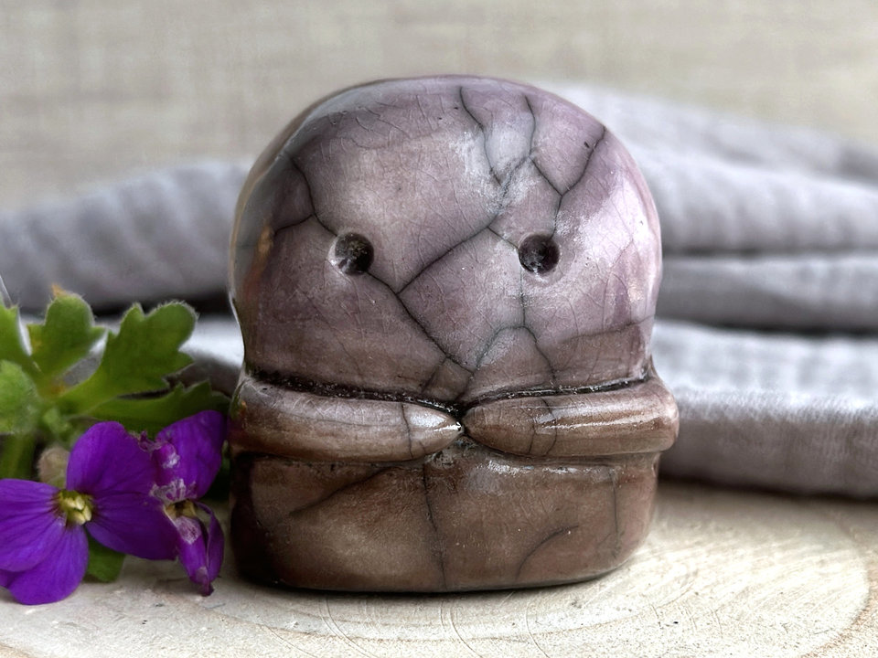 A kodama nature spirit ceramic guardian statue glazed in a bottom-to-top gradient of warm brown to soft mauve. It has a wide face, two big eyes, and cute little arms.