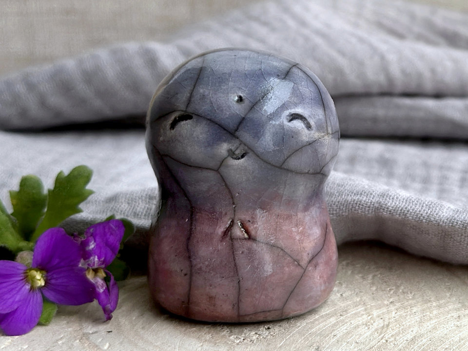 A smiley and loving Jizo Shinto raku ceramic sculpture talisman glazed in a bottom-to-top gradient of violet (with hints of soft orange) to blue. It has a kind, gentle face and is a wonderful smooth shape to hold in the hand.