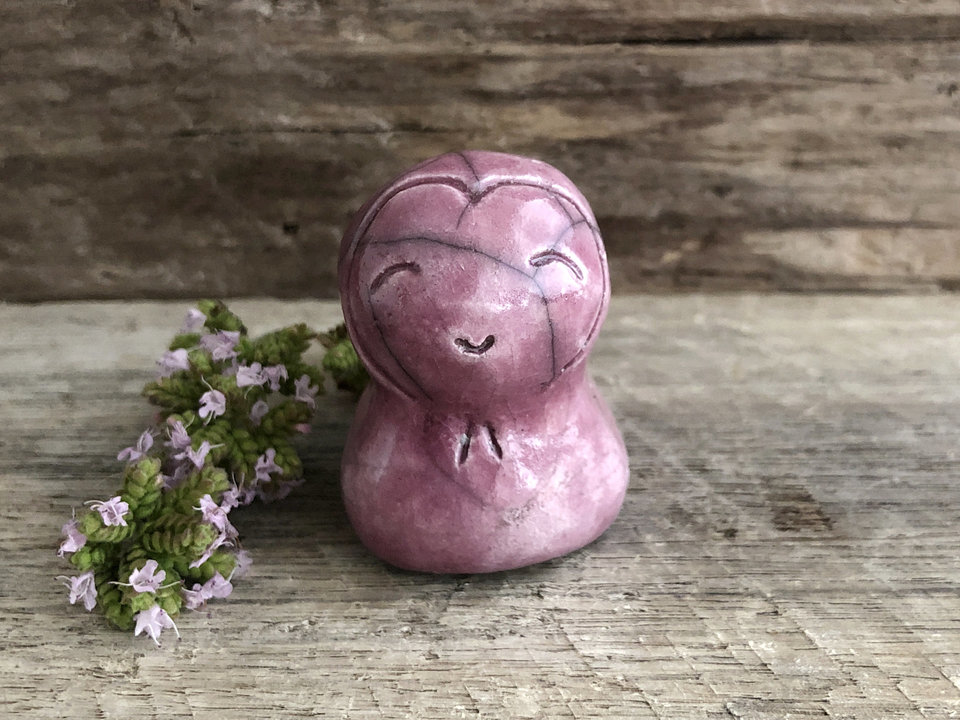 A smiley and loving Jizo Shinto raku ceramic sculpture talisman in soft deep pink with a heart shape around her kind, smiling face. A wonderful smooth shape to hold in the hand.