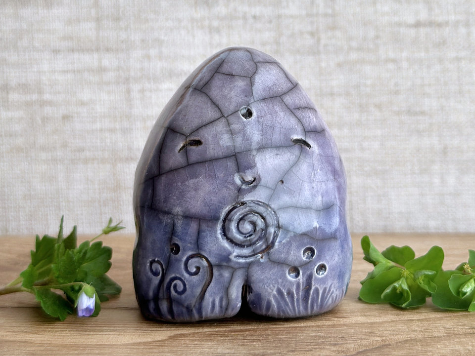 round and vaguely egg-shaped nature spirit sculpture. it is glazed in a bottom-to-top gradient of violet to purple and has spiral carvings on its body. it also has a gentle, happy face.