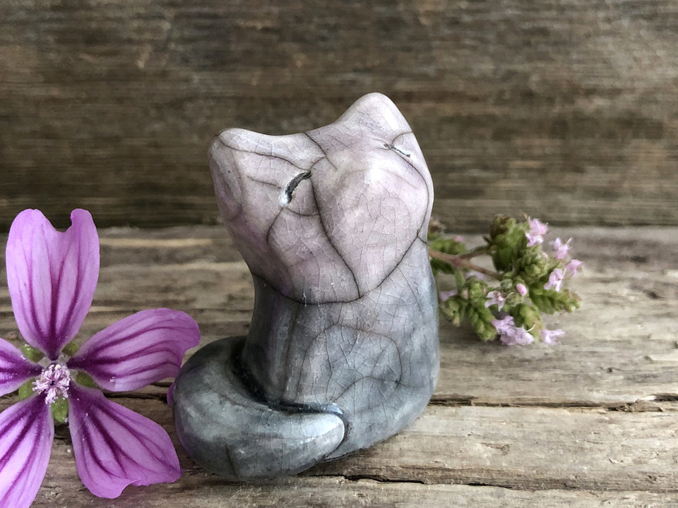 Raku ceramic sitting fox glazed in a soft gradient of grey-violet (at the bottom) to violet-mauve (at the top). His head is uplifted gently toward the sky, and he has a very sweet face.