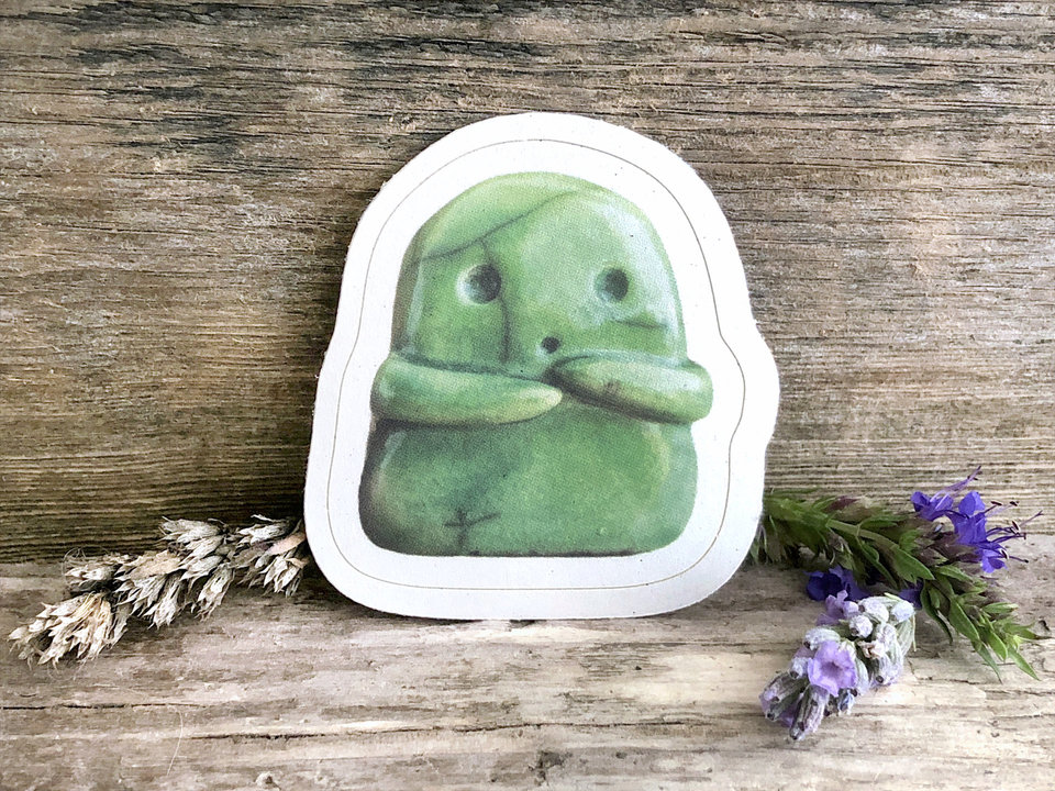 a sticker of a green ceramic kodama kami nature and tree spirit guardian. it has an sweet ooooo face and two little arms, and it's very cute! there is a thin white border all around the image.