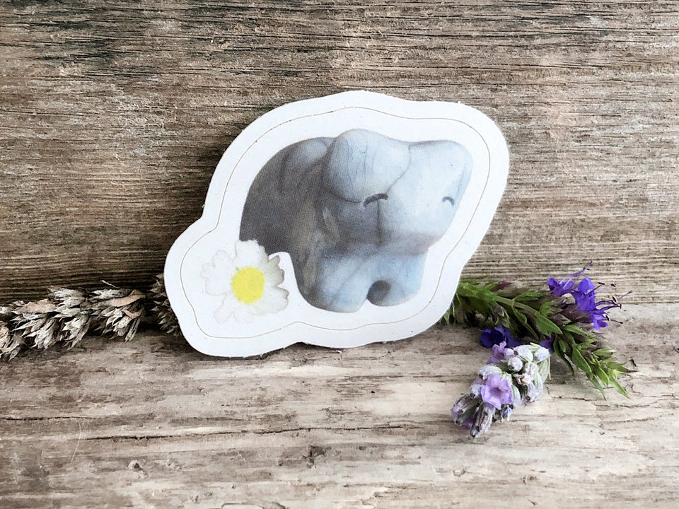 a sticker of a pale blue raku cermic bear sculpture. it has a sweet, friendly face, and there is a daisy next to it (part of the sticker). there is a thin white border around the image of bear and daisy.