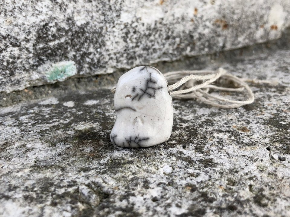 Simple raku ceramic Shinto Jizo pendant necklace glazed in white with amazing raku crackles. Jizo has a kind, happy face and is strung on a adjustable eco-hemp cord.
