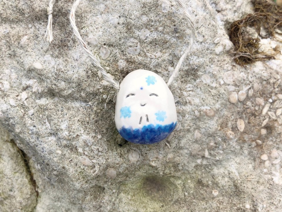 Ceramic Shinto Jizo pendant glazed in white with a blue winter snowflake design and a sweet smiling face.