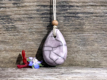 Raku ceramic worry pendant shaped a little like a bendy pear and glazed in pale purple. It has a sandalwood bead above it and is strung on a flax cord.