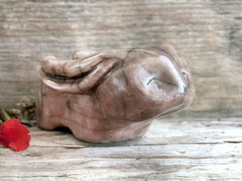 Raku ceramic sculpture of a rabbit. It is sitting with its long ears folded down its back and is glazed in dark, warm brown with a hint of rose pink up one side. It has a very sweet, gentle face.