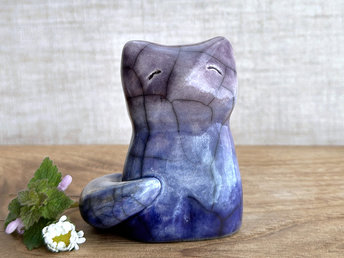 A calm and gentle Shinto Inari nighttime kitsune fox spirit ceramic raku statue glazed in a bottom-to-top gradient of dark blue to blue to purple. Its tail is curled around the right side of its body, and it has a kind face.