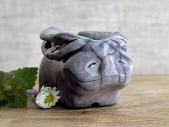 Raku ceramic sculpture of a rabbit. It is sitting with its long ears folded down its back and is glazed in a soft lavender colour. It has a very sweet, gentle face.