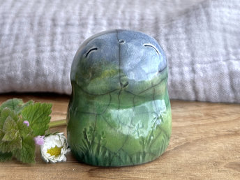 an earth elemental nature spirit ceramic sculpture. it is glazed in a bottom-to-top gradient of forest and spring green to blue and has plant and flower carvings on its body. it has a gentle, smiling face.
