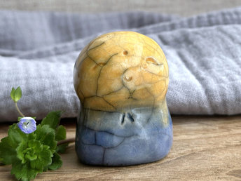 a smiley and loving Jizo Shinto raku ceramic sculpture talisman glazed in a bottom-to-top gradient of blue to golden yellow. they have a kind, gentle face and are a wonderful smooth shape to hold in the hand.
