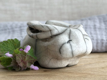 Raku ceramic sculpture of a rabbit. It is sitting with its long ears folded down its back and is glazed in white. It has a very sweet, gentle face.