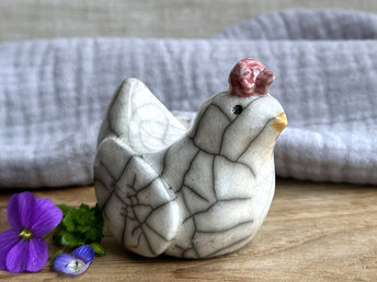 a white raku ceramic chicken with grey eyes, a pale orange beak, and a bordeaux red comb on the top of her head. she looks very sweet.
