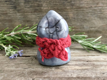 Raku ceramic spirit of winter glazed in a soft blue. It has a gentle face and a red, organic cotton crocheted scarf.