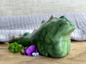 raku ceramic chunky dragon sculpture. it's glazed in green and has a very friendly face. it also has a long tail with little triangle bumps that run from the top of its head to the base of its tail; they're glazed in alternating forest green and soft red pink. 