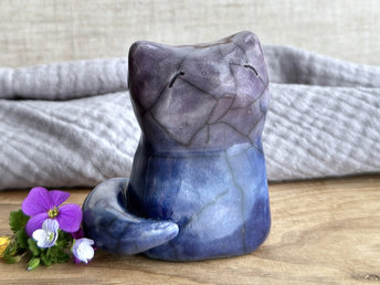 A calm and gentle Shinto Inari nighttime kitsune fox spirit ceramic raku statue glazed in a bottom-to-top gradient of dark blue to blue to purple. Its tail is curled around the right side of its body, and it has a kind face. There's a mild glaze disturbance pattern on its face that look like a little bit like where tiny snowflakes fell.