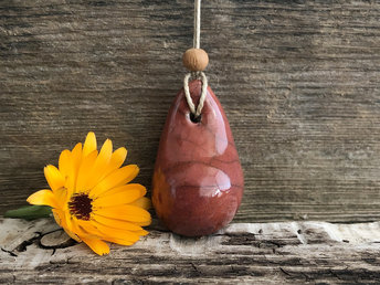 Raku ceramic worry pendant shaped a little like a bendy pear and glazed in a deep red-orange. It has a sandalwood bead above it and is strung on a flax cord.