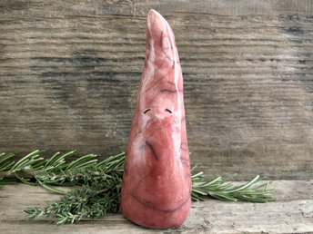 Raku ceramic sculpture of a tall, pointy gnome. He is very friendly and glazed in a warm, soft red colour.
