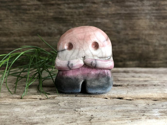 A sweet little nature spirit ceramic guardian statue glazed in the genderfluid pink, white, purple, black, and blue colours and with a lovely, gentle face and little arms. It has a small branch design carved up one side.