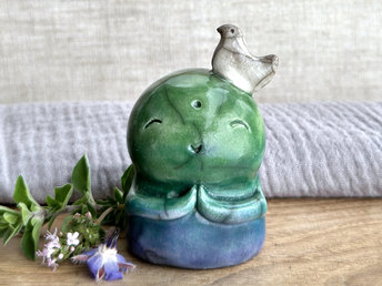a raku ceramic jizo nature spirit guardian sculpture glazed in a bottom-to-top gradient of blue to forest green to spring green. they have a happy, smiley face, little praying hands, and a sweet white bird on their head.